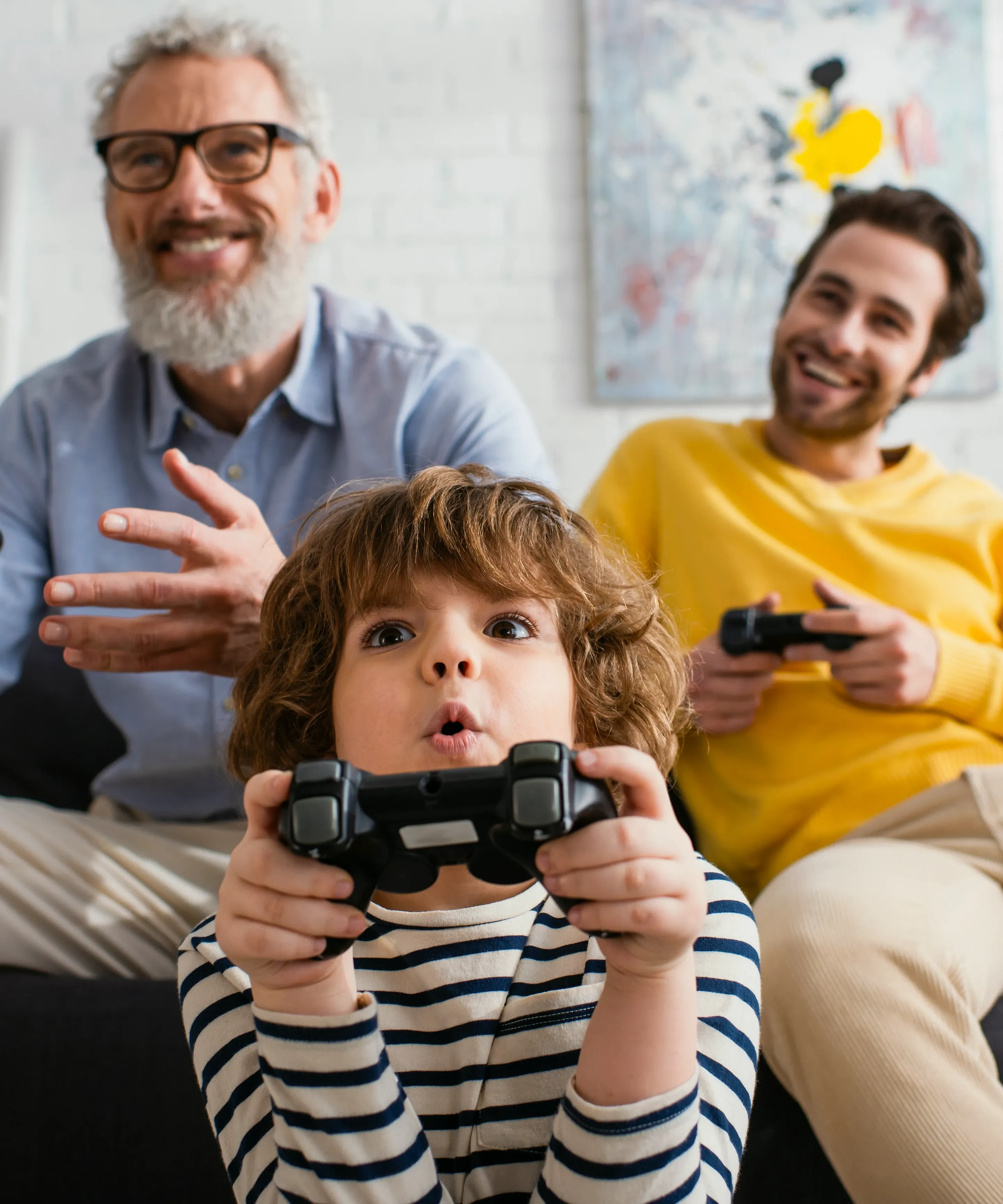 Familie spielt mit einer Spielekonsole im Wohnzimmer. Es ist ein Großvater mit Sohn und Enkel zu sehen. 
